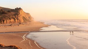 A beach with cliffs, a sandy shore, and two people walking. - Experience the perfection of Half Moon Bay Oasis By Pillar Point Beach! (El granada)