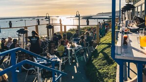 An outdoor dining area with tables and chairs, overlooking a body of water with boats. - Experience the perfection of Half Moon Bay Oasis By Pillar Point Beach! (El granada)