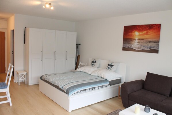 Une chambre à coucher avec un lit, une armoire blanche, un canapé marron et un tableau représentant un coucher de soleil.