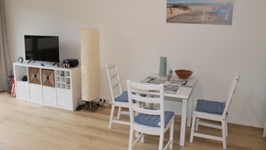 A living room with a TV, white furniture, a painting, and a wooden floor.