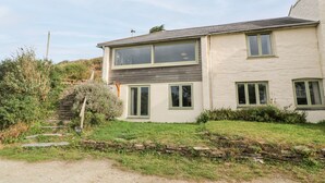 A two-story house with a stone staircase leading up to the entrance, surrounded by greenery. - Porth Farm Annexe (Newquay)