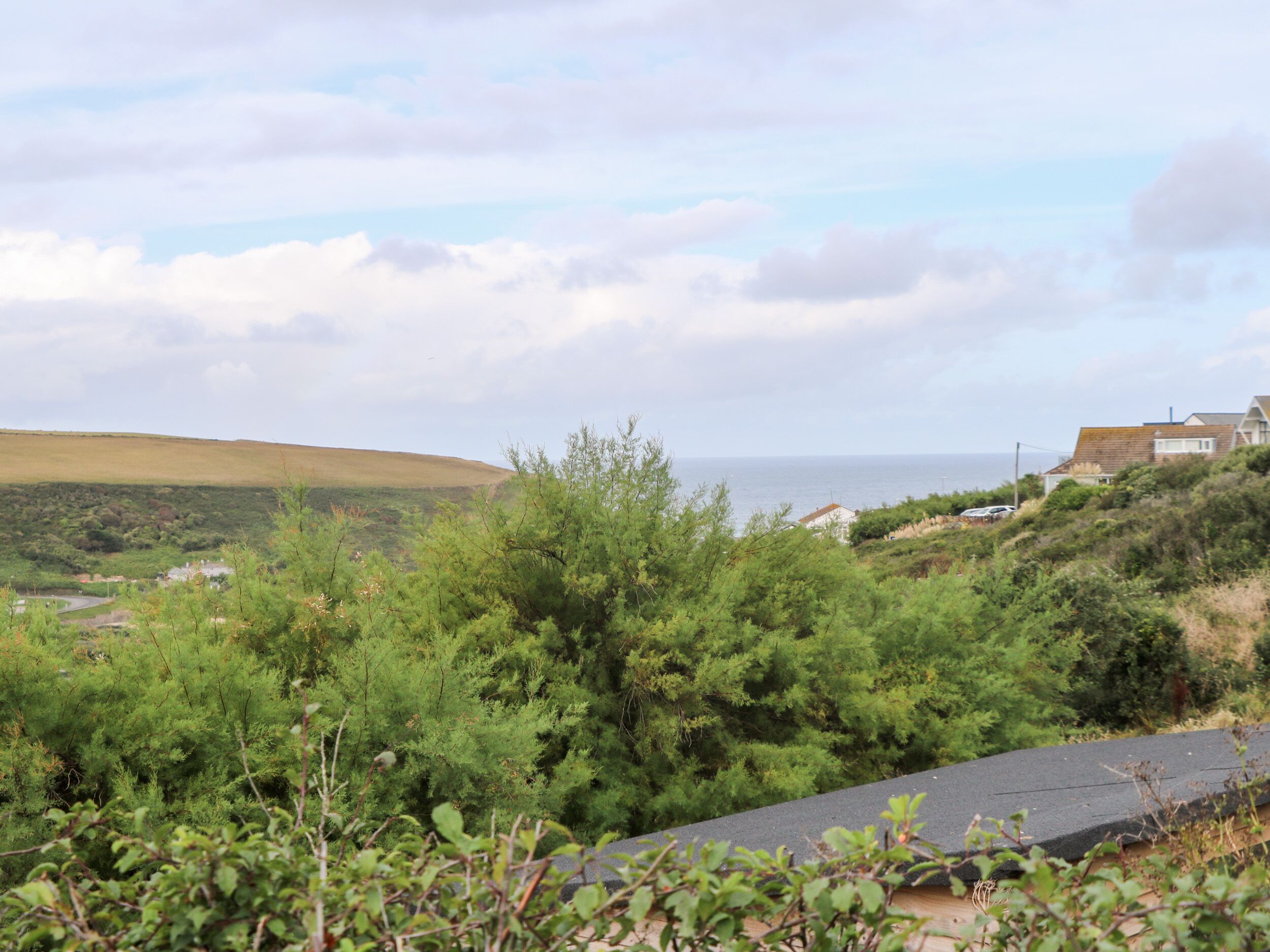 Eine Küstenlandschaft mit Blick aufs Meer, einem grasbewachsenen Hügel und einem Haus mit schrägem Dach.