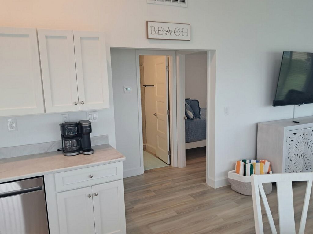 A modern kitchen with white cabinets, a coffee maker, and a sign above the door that reads 'BEACH'.