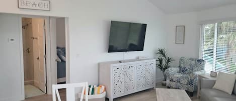 A living room with a television, a white cabinet, a patterned armchair, and a sofa.