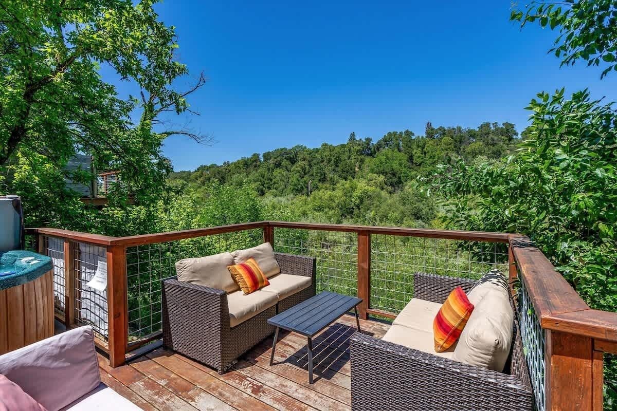 An outdoor deck with wicker furniture, a small table, and a view of a forested area.