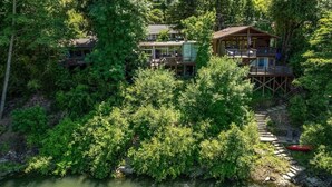 Una cabana amb terrassa, envoltada per un bosc dens i un riu.