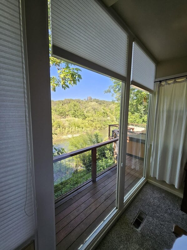 A room with a large sliding glass door leading to a balcony with a view of a river and forested hills.