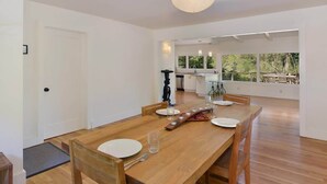 Un coin repas avec une table en bois, des chaises et une vue sur la cuisine et la terrasse extérieure.