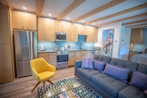 Una cocina moderna con armarios de madera, electrodomésticos de acero inoxidable y una zona de comedor con sofá y cojines.