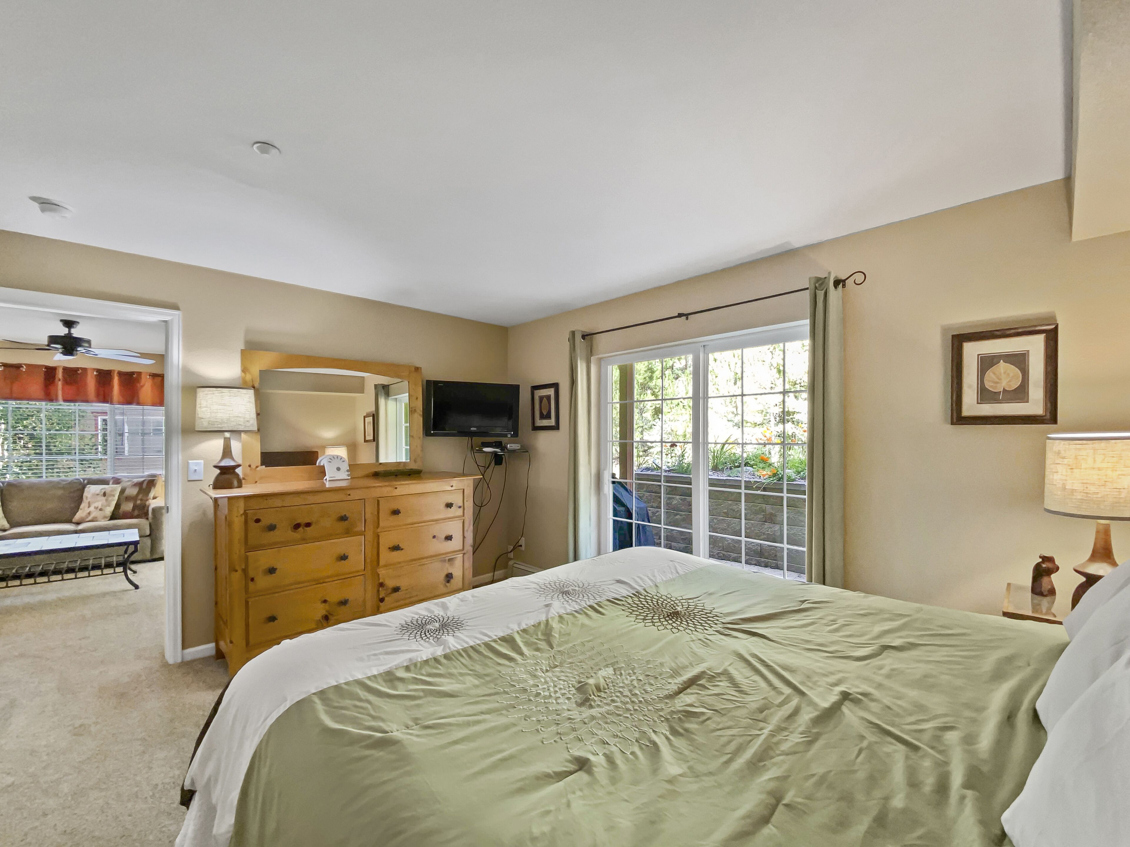 A bedroom with a bed, dresser, television, and a window with curtains.