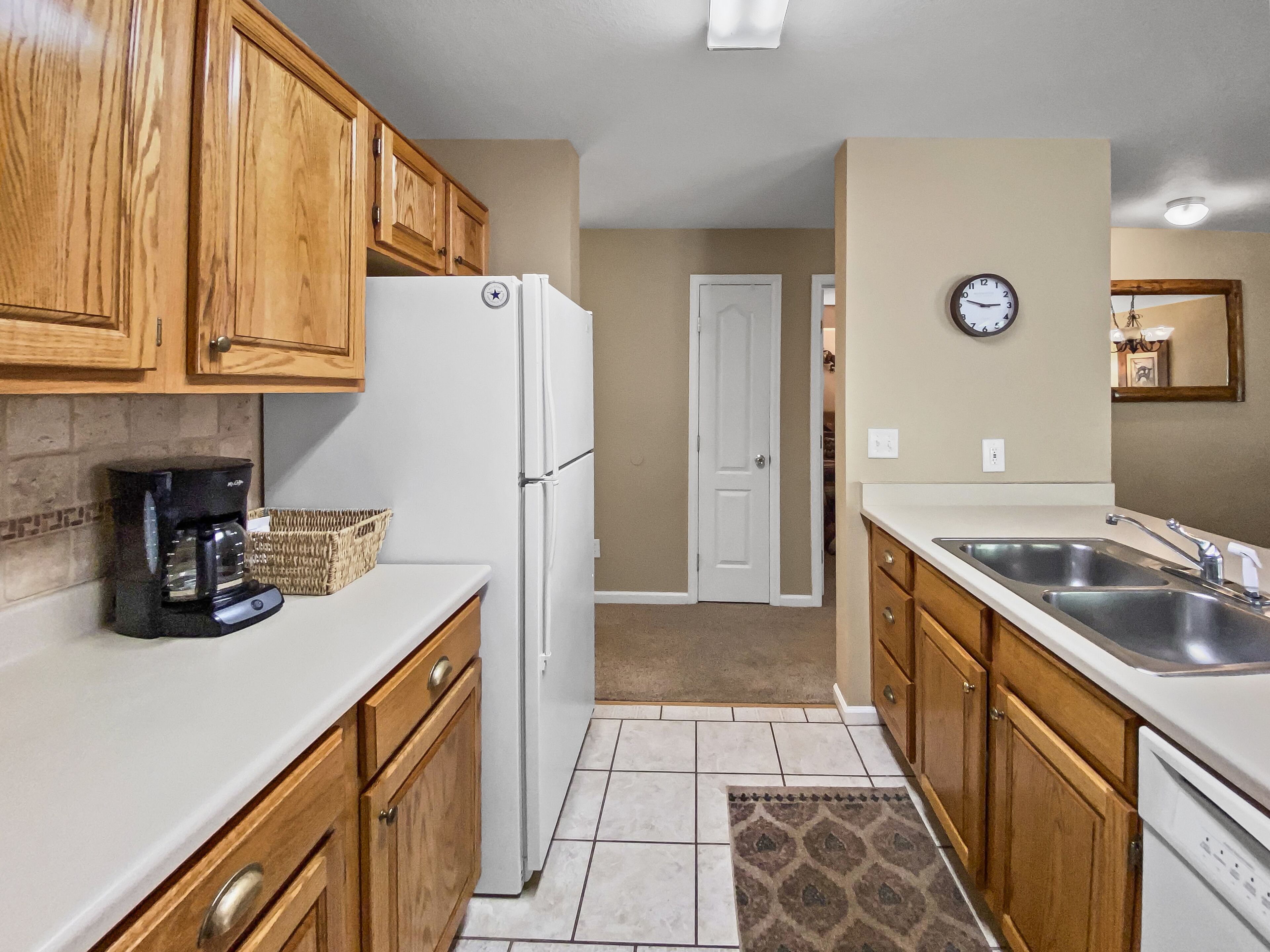 A kitchen with wooden cabinets, a white refrigerator, a coffee maker, a sink, and a clock on the wall.