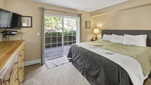 A bedroom with a bed, a TV, a desk, and a sliding glass door leading to a balcony.