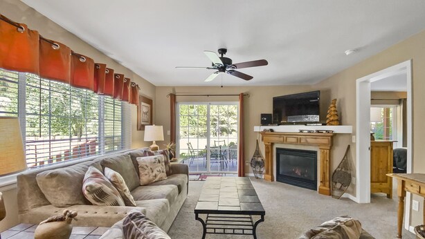 A spacious living room with a sofa, coffee table, and fireplace. There is a television mounted above the fireplace and a ceiling fan.