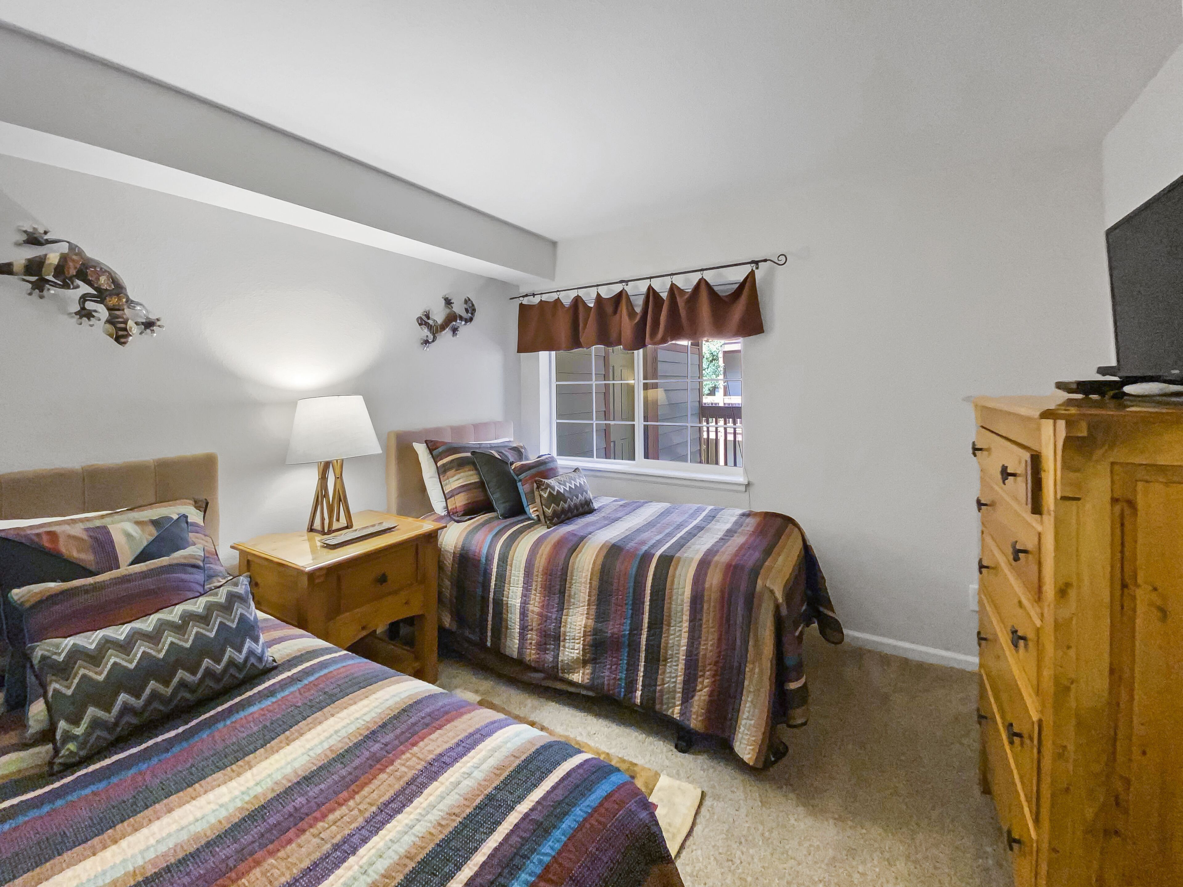 A bedroom with two beds, a wooden dresser, a TV, and a window with curtains.