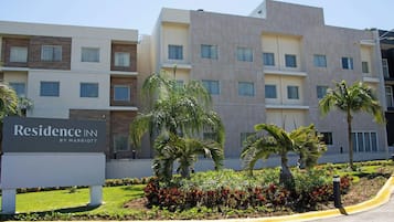 A multi-story hotel with a sign reading "Residence Inn by Marriott" and a landscaped garden with palm trees and shrubs.