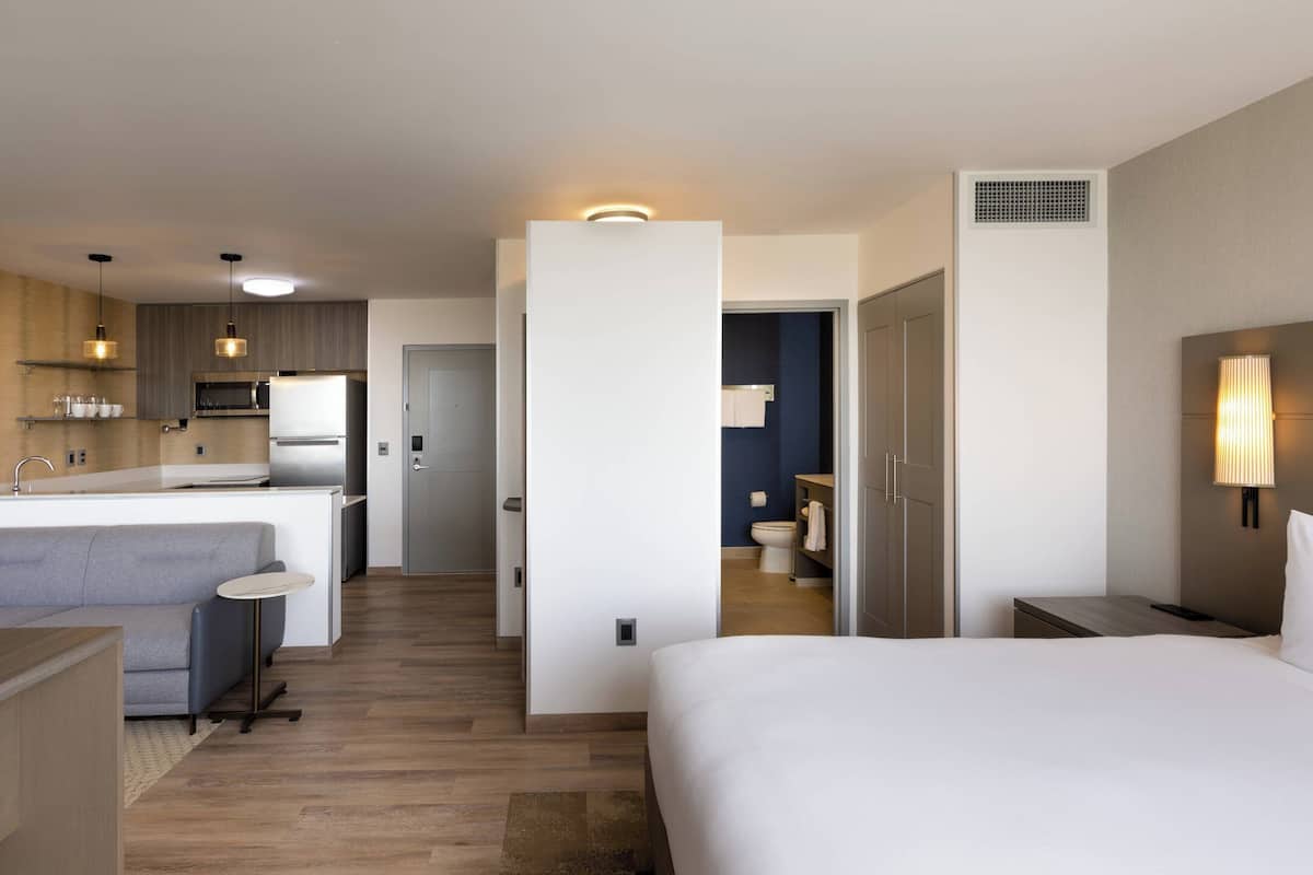 Una habitación de hotel moderna con kitchenette, baño independiente y una cama grande.