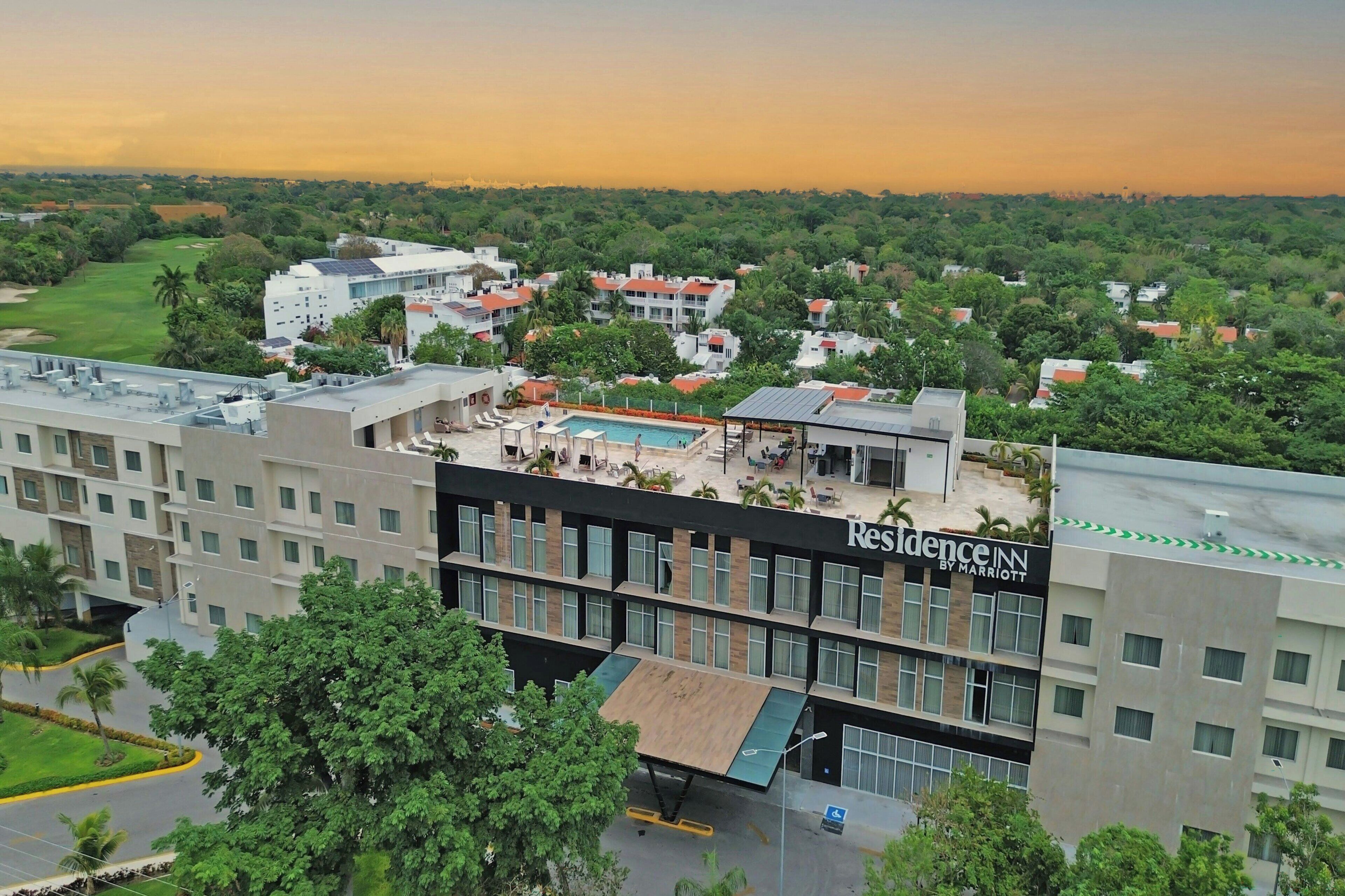 Un hôtel doté d’une piscine sur le toit, entouré de verdure et d’immeubles d’habitation.