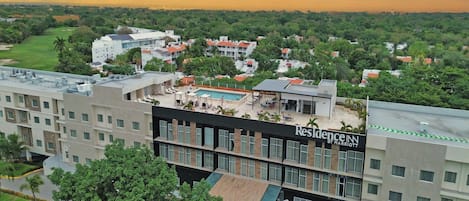 A hotel with a rooftop pool, surrounded by greenery and residential buildings.