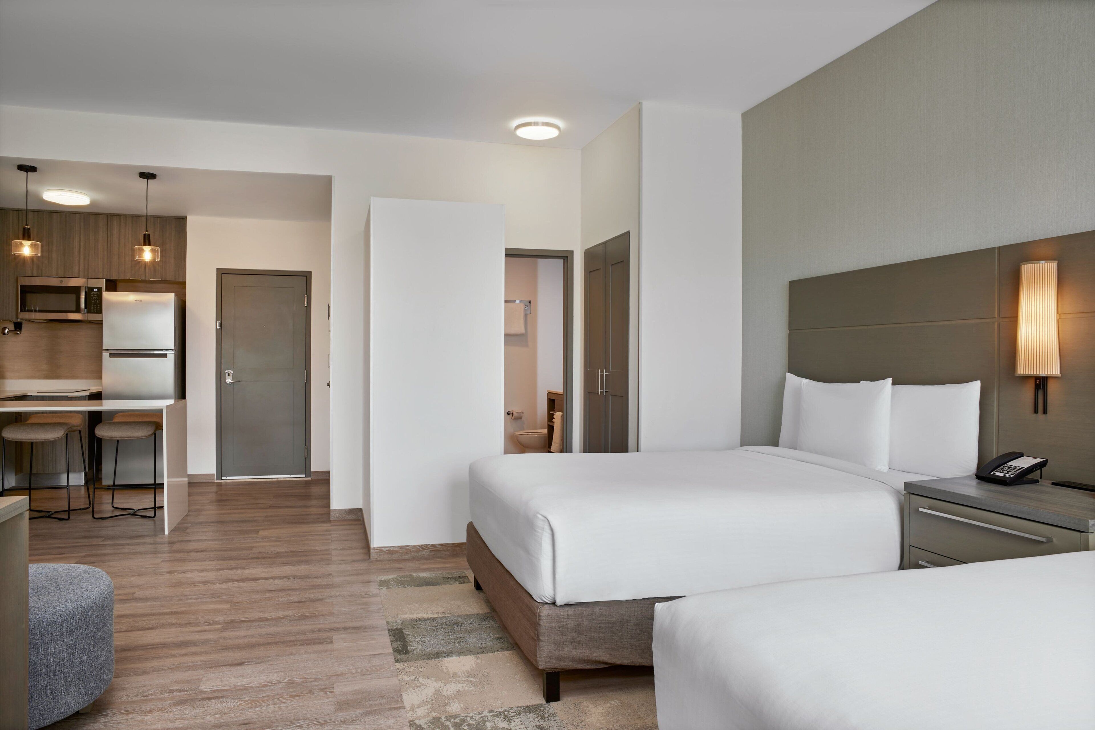 Habitación de hotel con dos camas, un escritorio con silla, microondas y refrigerador.