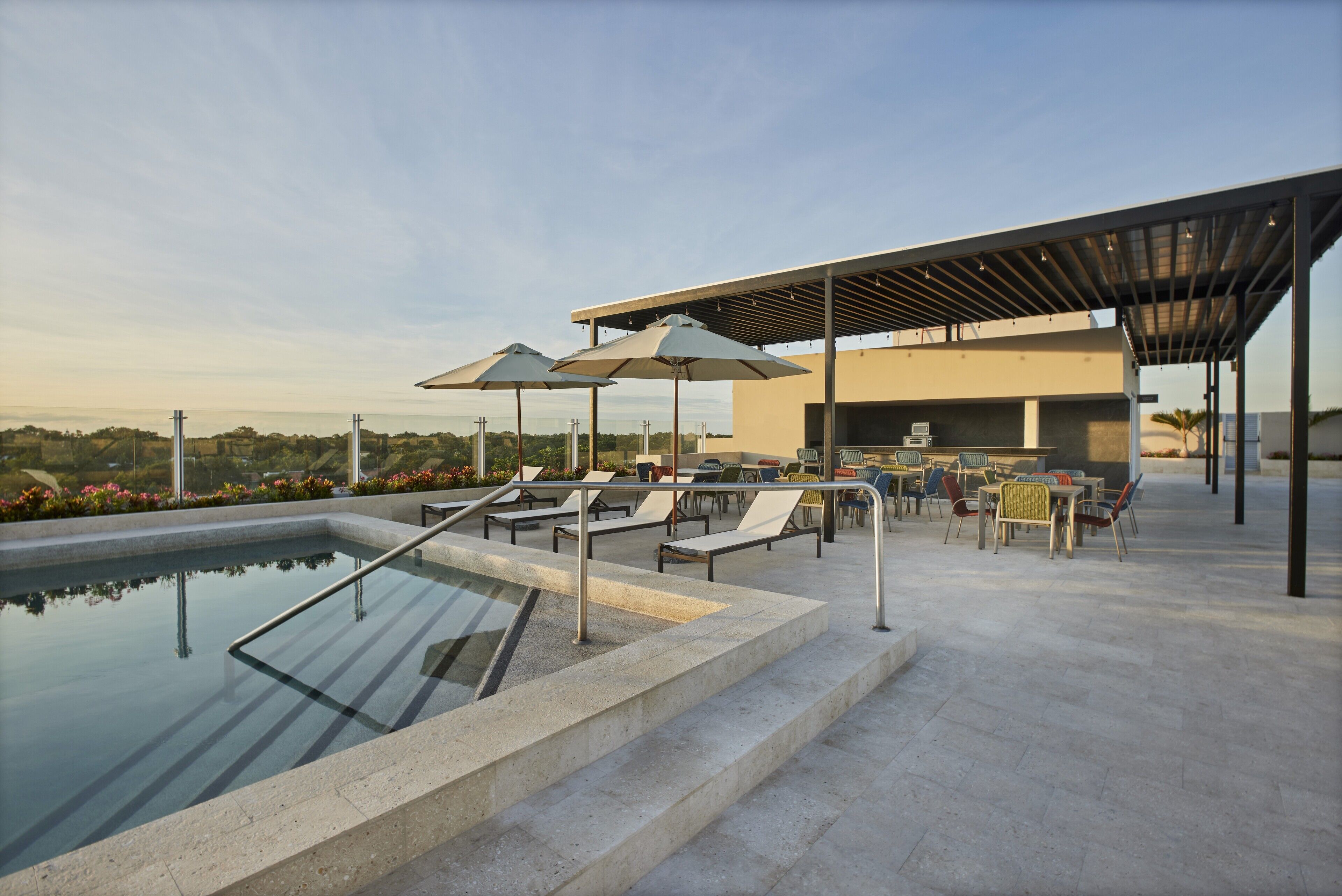 A rooftop pool area with lounge chairs and umbrellas, a covered seating area, and a view of the landscape.