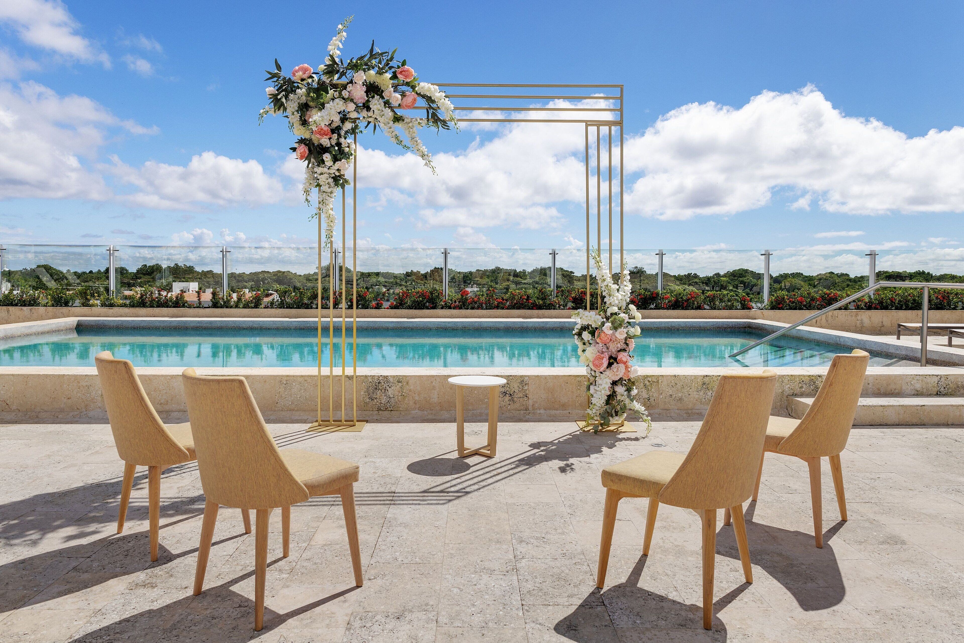 An outdoor seating area with a pool view, a floral arch, and a clear sky.