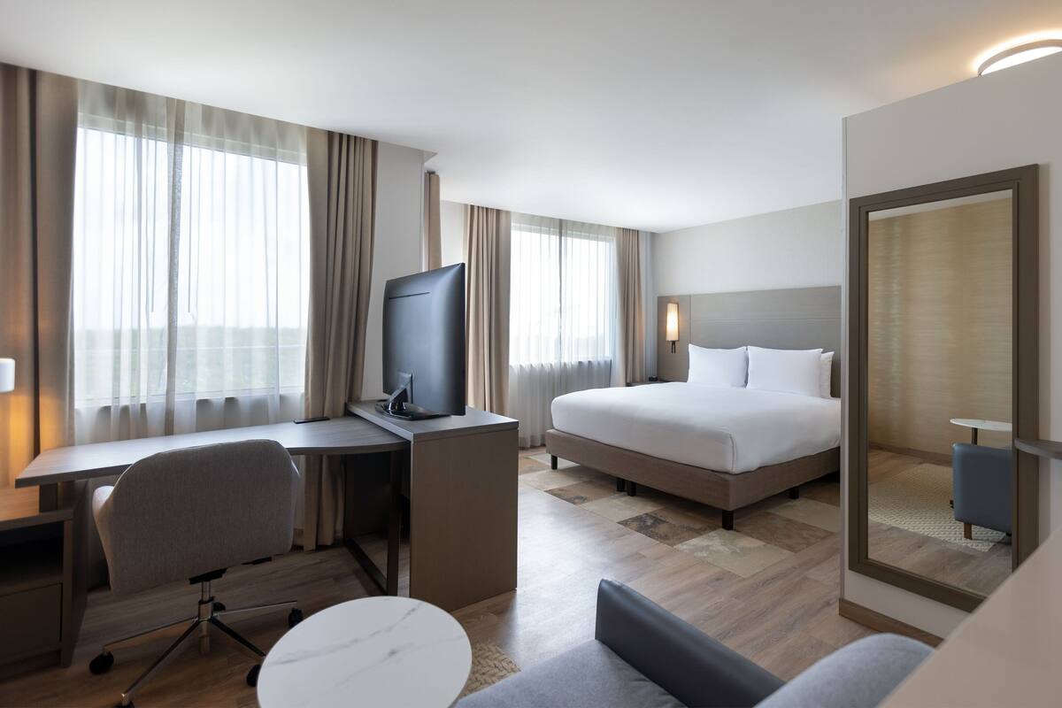 Una habitación de hotel con cama, escritorio, silla, televisor y una pequeña mesa.