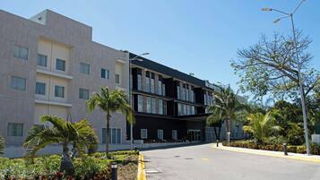 Un hotel moderno con una estructura de dos pisos, un acceso cubierto y un área ajardinada con palmeras y arbustos.