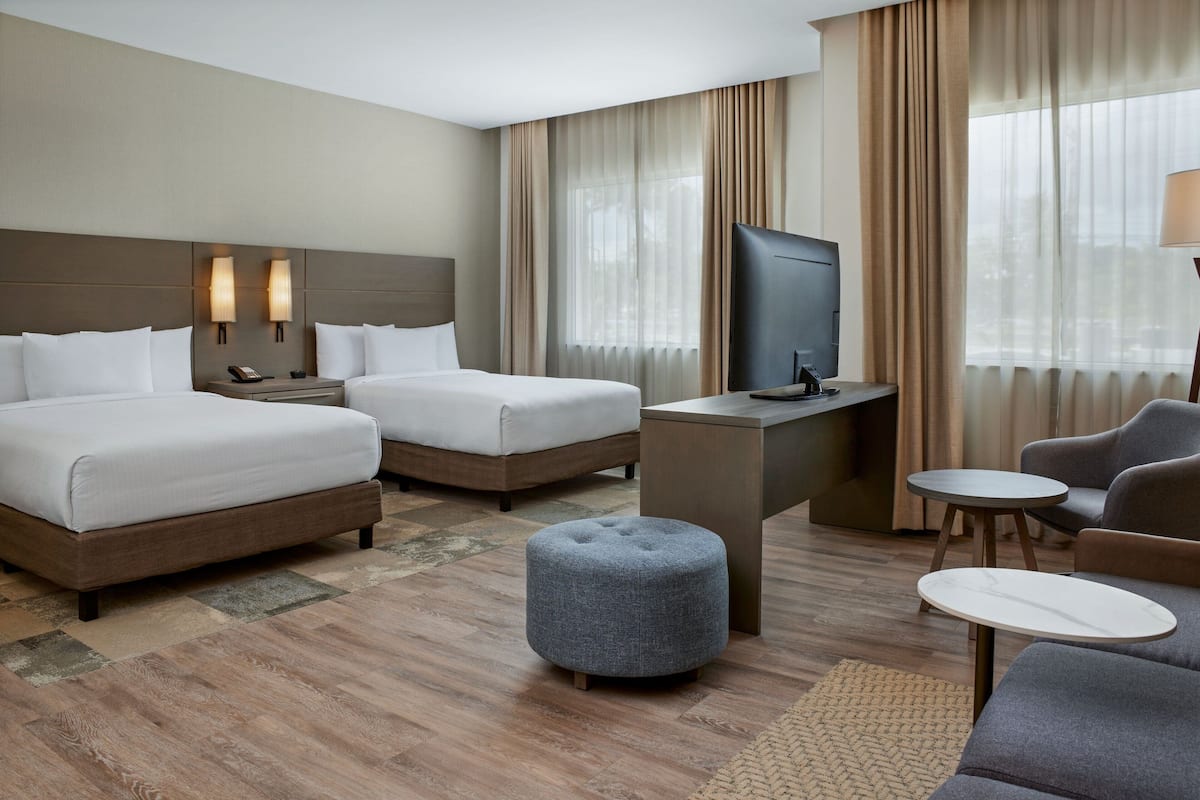 Habitación de hotel con dos camas, televisión, escritorio y zona de estar.
