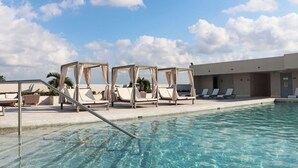 Zona de piscina amb aigua cristal·lina, gandules i zona de seients coberta.