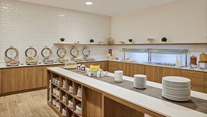 Montaje de bufé con varias estaciones de servicio, una barra central y una gran variedad de alimentos.