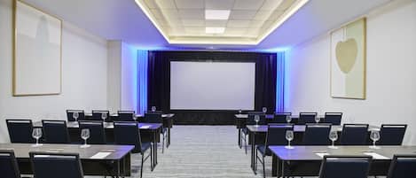 A conference room with tables and chairs, a large screen, and a carpeted floor.