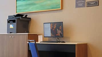 A hotel reception desk with a computer monitor displaying room information, a printer, and a framed painting on the wall.