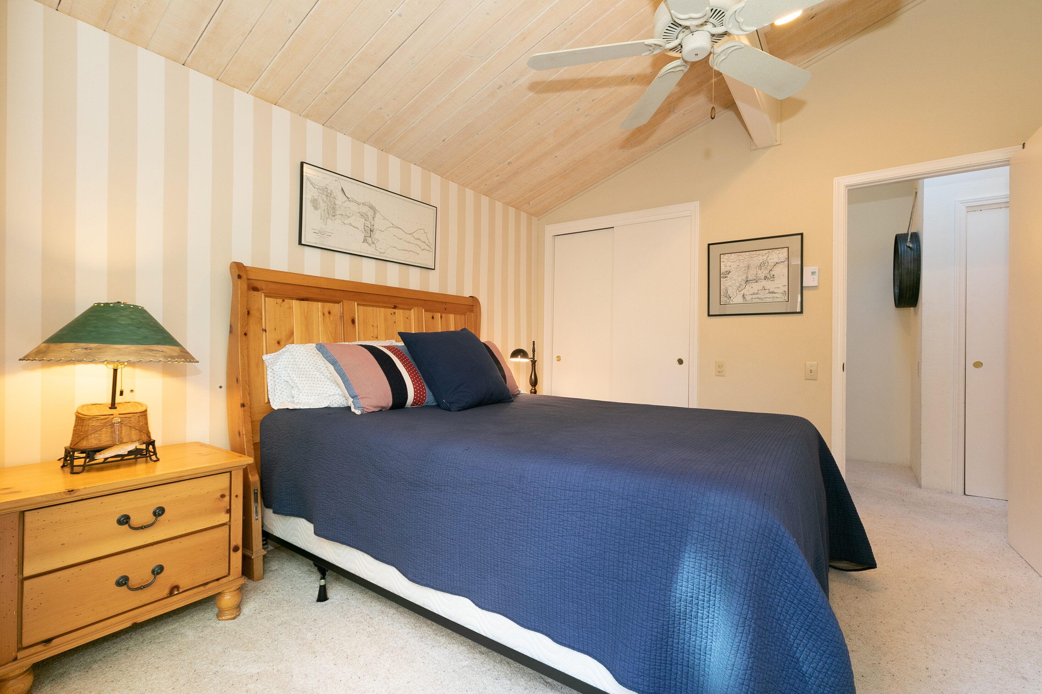 A bedroom with a wooden bed, striped wallpaper, a ceiling fan, and a nightstand with a lamp.
