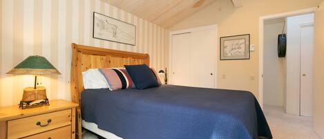 A bedroom with a wooden bed, striped wallpaper, a ceiling fan, and a nightstand with a lamp.