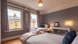 A bedroom with two beds, a desk, and a chair. There are curtains on the windows, and a lamp on the desk.