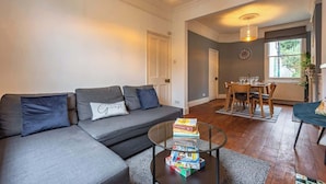 A modern living room with a grey sofa, a glass coffee table, and a dining area with a wooden table and chairs.