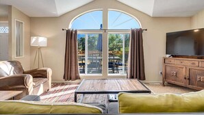 A living room with a large arched window, a sofa, a coffee table, a TV, and a wooden cabinet. - Calistoga Vineyard Getaway - Hot Tub and Tastings Included (Calistoga)