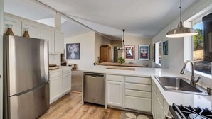 A modern kitchen with white cabinetry, stainless steel appliances, a dishwasher, and a large window providing natural light. - Calistoga Vineyard Getaway - Hot Tub and Tastings Included (Calistoga)