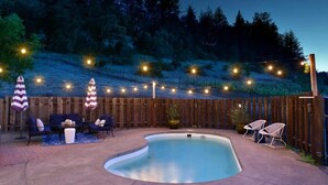 A backyard with a swimming pool, outdoor furniture, string lights, and a wooden fence. - Calistoga Vineyard Getaway - Hot Tub and Tastings Included (Calistoga)