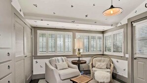 A room with a sofa, armchair, and a small table with a lamp. There are windows with shutters, a ceiling with bird decals, and a door with a handle. - Healdsburg Plaza Gem-Hot Tub and Tastings Included (Healdsburg)