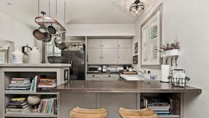 A compact kitchen with a central island, bar stools, a bookshelf, and a hanging pot rack. - Healdsburg Plaza Gem-Hot Tub and Tastings Included (Healdsburg)