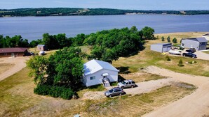 A lakeside property with a white house, a barn, and several vehicles.