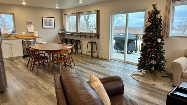 A spacious living area with a leather couch, a dining table with chairs, a kitchen area, and a Christmas tree.