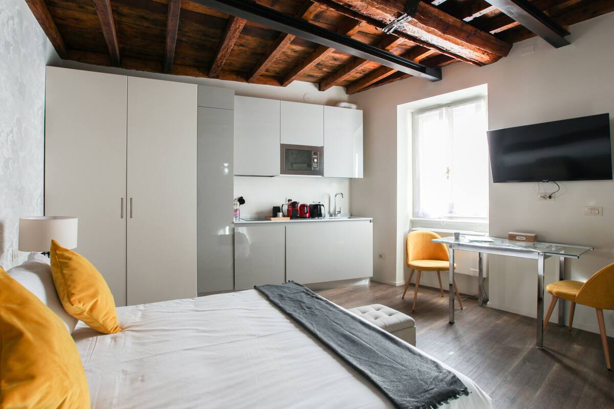 A bedroom with a bed, a desk, and a kitchenette.