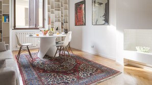 Una sala moderna con un sofá blanco, una mesa de comedor con sillas, una alfombra estampada y una chimenea blanca.