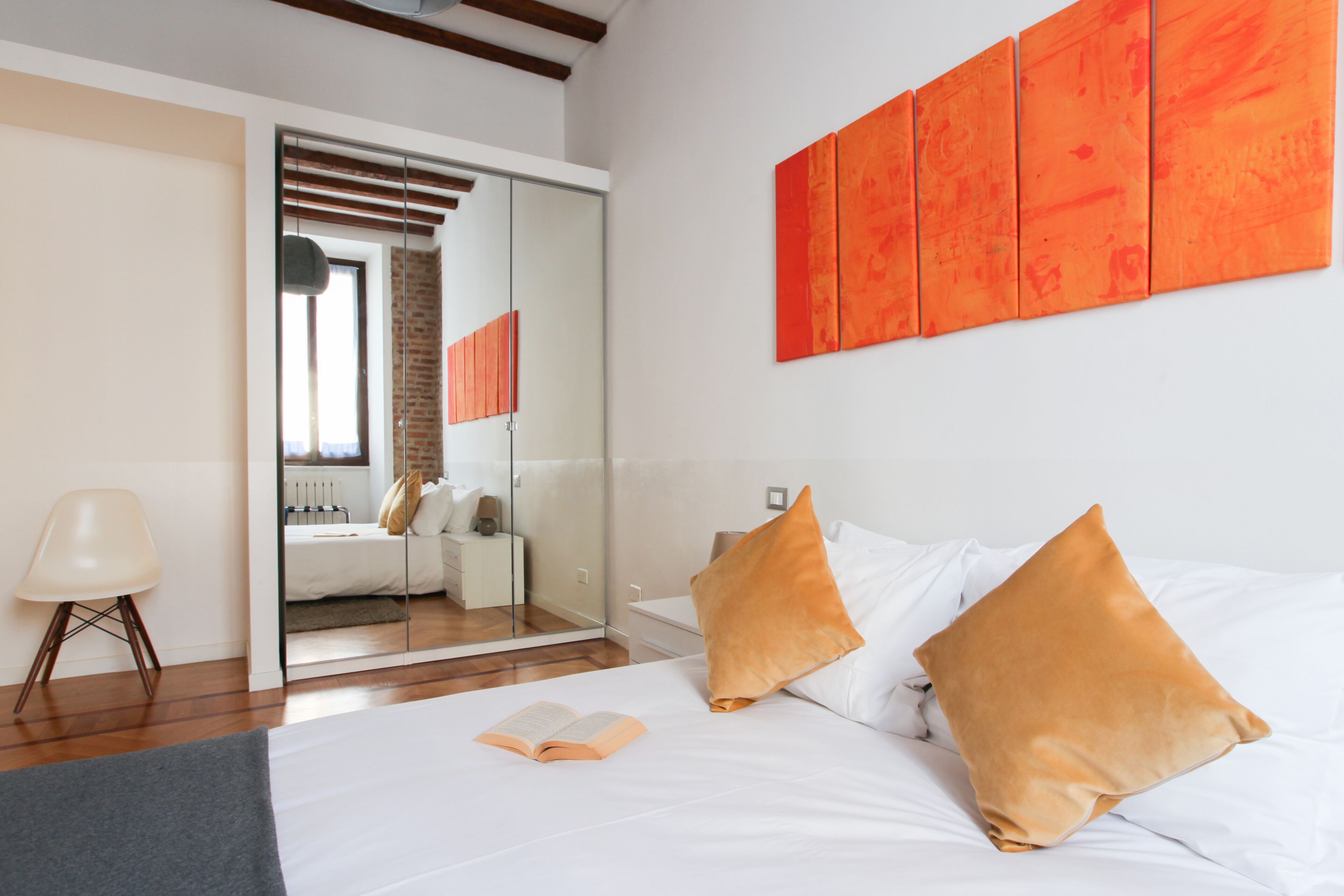 Une chambre à coucher moderne avec un grand lit, deux oreillers, un livre et un miroir qui reflète une salle de bain.