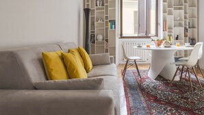 Una sala de estar con un sofá gris, cojines amarillos, una mesa de centro blanca y un tapete estampado.