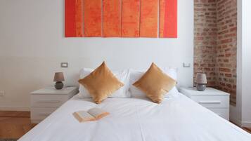 Una cama bien hecha con dos almohadas, una mesita de noche con lámpara y una pared con cinco paneles anaranjados.