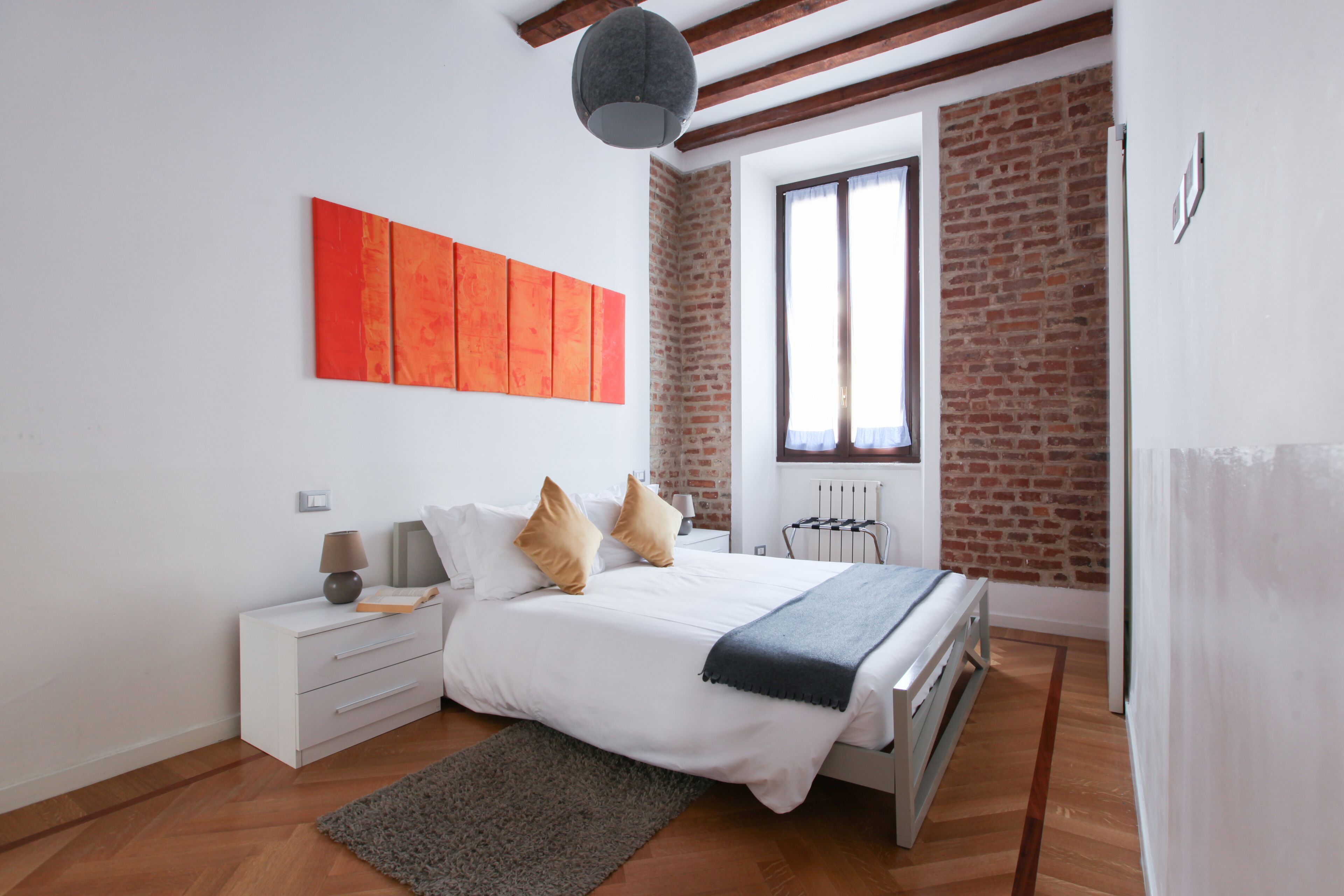 A modern bedroom with a bed, white nightstands, a grey rug, and a brick wall.
