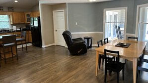 A modern kitchen with wooden cabinets, a black refrigerator, and a dining area with a wooden table and black chairs. - Lake Retreat House (Anderson)